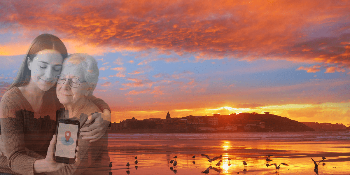 plan-geolocalizacion-alzheimer-gijon (1) Joven abraza con ternura a su abuela con Alzheimer mientras muestra una app de geolocalización en un móvil, sobre el fondo del atardecer en la playa de San Lorenzo de Gijón, símbolo de protección, cariño y seguridad para nuestros mayores.